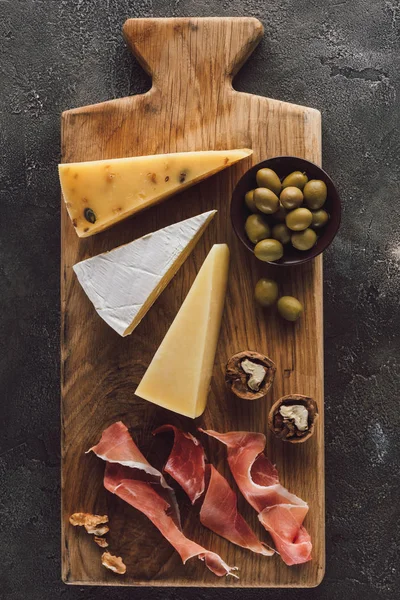 Posa piatta con formaggio assortito, marmellata e olive in ciotola su superficie scura — Foto stock