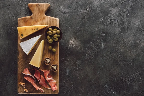 Posa piatta con formaggio assortito, marmellata e olive in ciotola su superficie scura — Foto stock