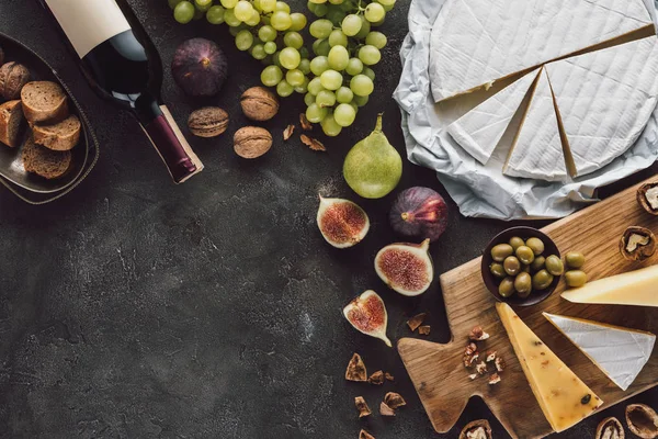 Draufsicht auf verschiedene Käsesorten, eine Flasche Wein und Früchte auf einer dunklen Tischplatte — Stockfoto