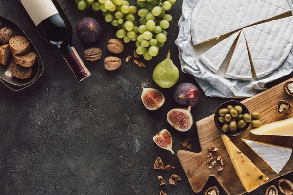 Top view of assorted cheese, bottle of wine and fruits on dark tabletop — Stock Photo