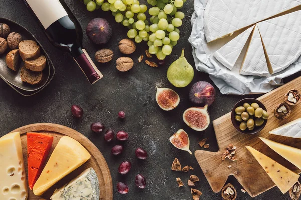 Vista superior del surtido de quesos, botellas de vino y frutas en la mesa oscura - foto de stock