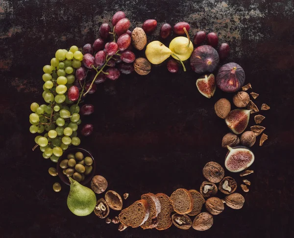 Tendido plano con varias frutas, trozos de pan y avellanas surtidos en círculo sobre la mesa oscura - foto de stock