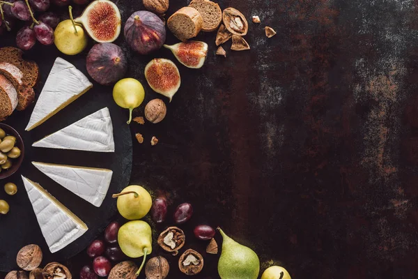 Вид сверху на кусочки сыра камамбер и фрукты, расположенные на темной поверхности — стоковое фото