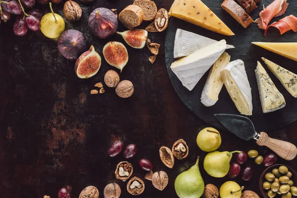 Flat lay with assorted cheese, hazelnuts and fruits on dark surface — Stock Photo