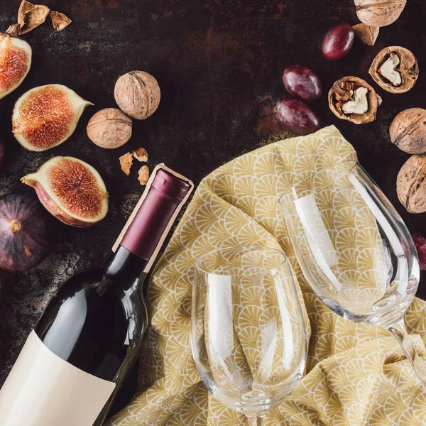 Top view of bottle of wine, empty glasses, hazelnuts and figs on dark tabletop — Stock Photo