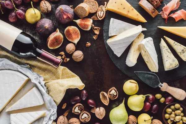 Composizione alimentare con formaggio, bottiglia di vino e frutta su tavolo scuro — Foto stock