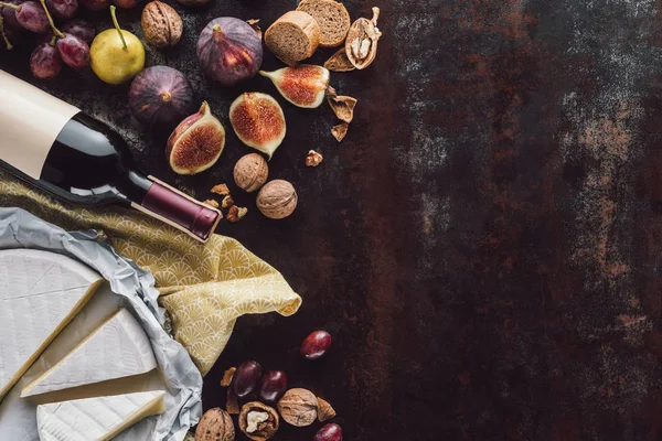 Composizione alimentare con formaggio, bottiglia di vino e frutta su tavolo scuro — Foto stock