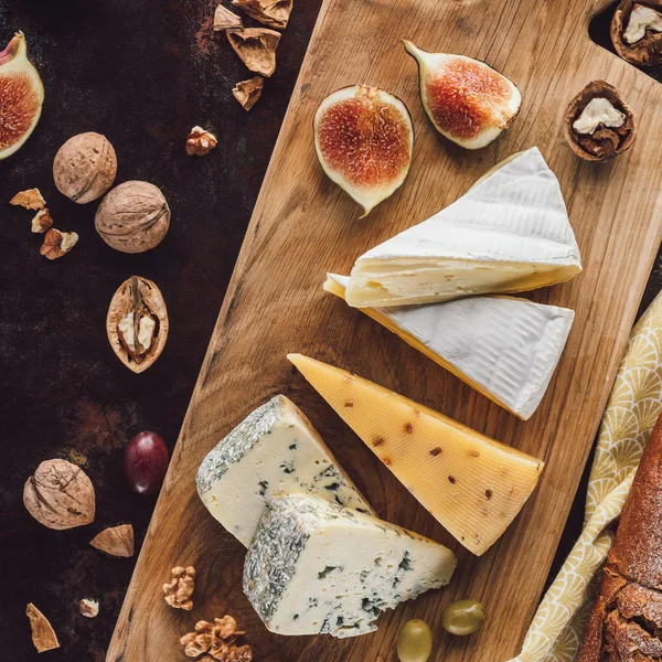 Food composition with assorted cheese, figs and hazelnuts on dark tabletop — Stock Photo