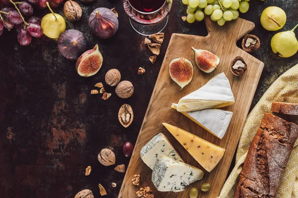 Essenszusammensetzung mit verschiedenen Käsesorten, einem Glas Wein und Früchten auf dunkler Tischplatte — Stockfoto