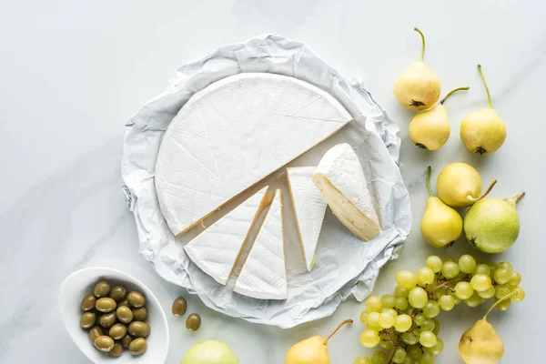 Flat lay with camembert cheese, olives and fruits on white marble surface — Stock Photo
