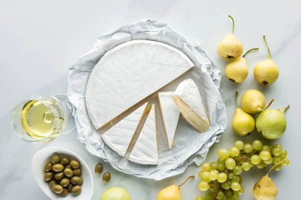 Flat lay com copo de vinho, queijo brie, azeitonas e frutas na superfície de mármore branco — Fotografia de Stock