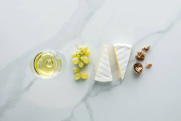 Flat lay with glass of wine, camembert cheese and hazelnuts on white marble surface — Stock Photo