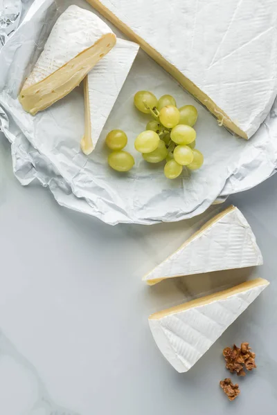 Flat lay with camembert cheese, hazelnuts and grape on white marble surface — Stock Photo