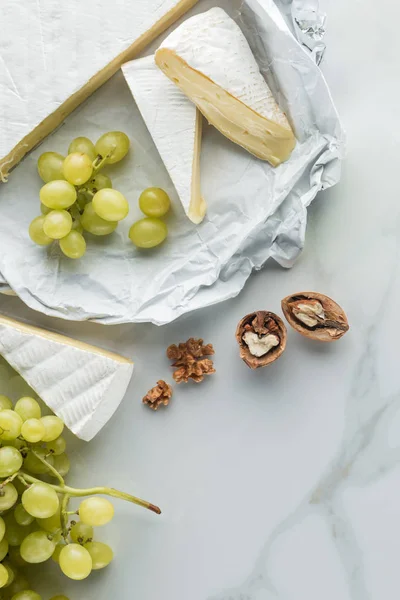 Flat lay with camembert cheese, hazelnuts and grape on white marble surface — Stock Photo