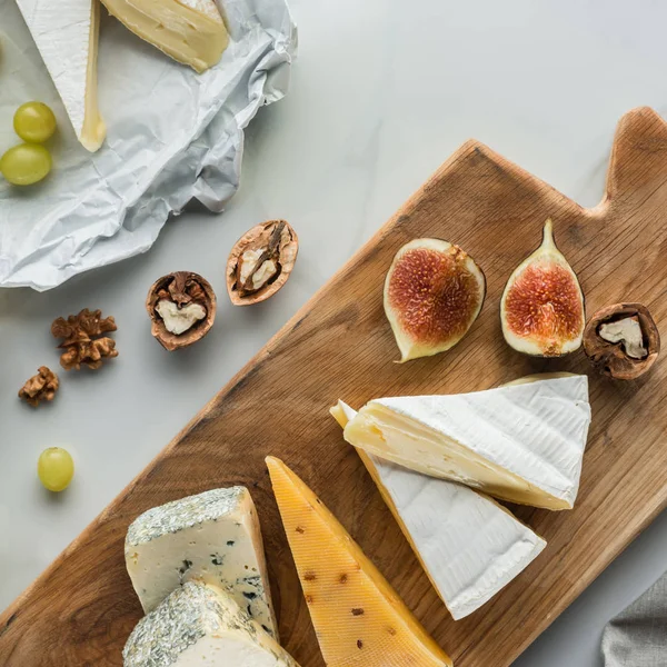 Flat lay with food composition of cheese and fig pieces on cutting board on white marble surface — Stock Photo