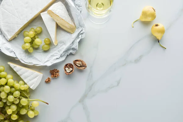 Tendido plano con copa de vino, queso camembert, peras y uva en la superficie de mármol blanco - foto de stock
