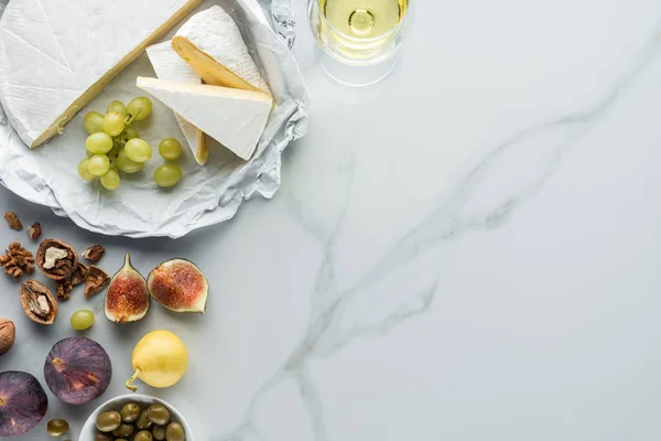 Plat avec olives, fromage camembert, vin et fruits disposés sur la surface de marbre blanc — Photo de stock