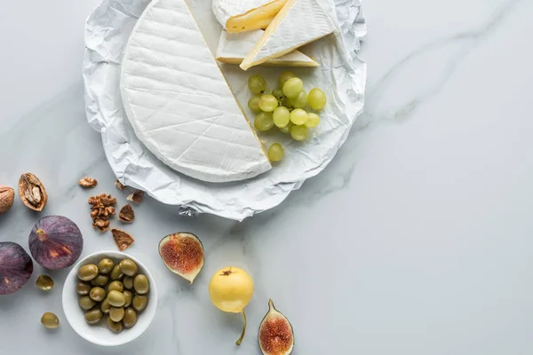 Plat avec des olives, du fromage camembert et des fruits disposés sur la surface de marbre blanc — Photo de stock