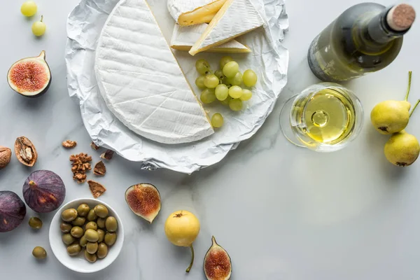 Plat avec olives, fromage camembert, vin et fruits disposés sur la surface de marbre blanc — Photo de stock