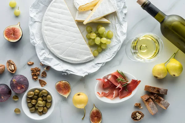 Flat lay with wine, camembert cheese, jamon, figs, grape and bread on white marble tabletop — Stock Photo