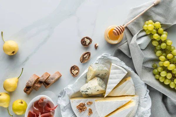 Flat lay com mel, queijo, jamon, avelãs e uva dispostos em mesa de mármore branco — Fotografia de Stock
