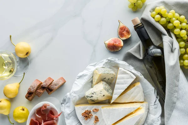 Flat lay com vinho, queijo, jamon e frutas dispostas em mesa de mármore branco — Fotografia de Stock