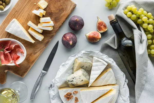 Flat lay com vinho, queijo, jamon, figos e uva dispostos em mesa de mármore branco — Fotografia de Stock