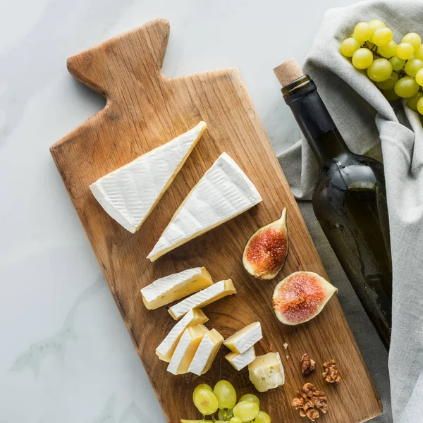 Yacía plana con la composición de alimentos de queso camembert en la tabla de cortar y el vino en la superficie de mármol blanco - foto de stock