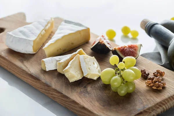 Vista de cerca de los trozos de queso camembert, uva e higo en la tabla de cortar en la mesa blanca - foto de stock