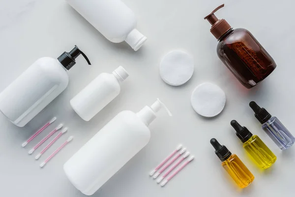 Top view of bottles of cream, natural oils and cosmetic pads on white surface, beauty concept — Stock Photo
