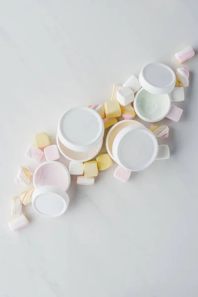 Vista elevada de garrafas de creme e marshmallows na superfície branca, conceito de beleza — Fotografia de Stock