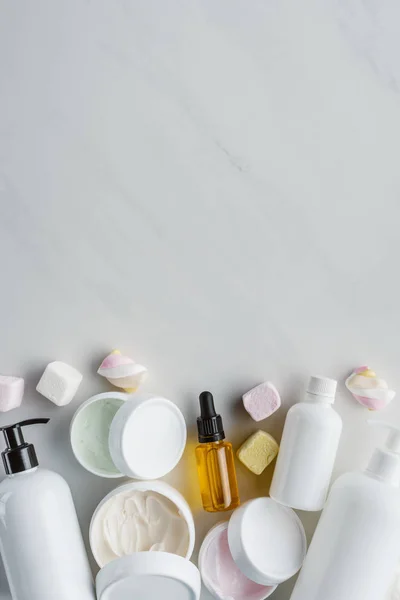 Elevated view of bottles of cream, natural oils and marshmallows on white surface, beauty concept — Stock Photo