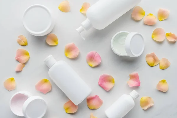 Vista elevada de botellas de crema y pétalos de rosa sobre mesa blanca, concepto de belleza - foto de stock