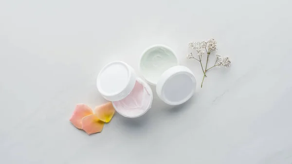 Vue du dessus des bouteilles de crème, fleurs séchées et pétales de rose sur surface blanche, concept beauté — Photo de stock