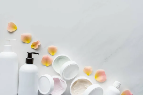 Vista superior de botellas de crema y pétalos de rosa sobre mesa blanca, concepto de belleza - foto de stock