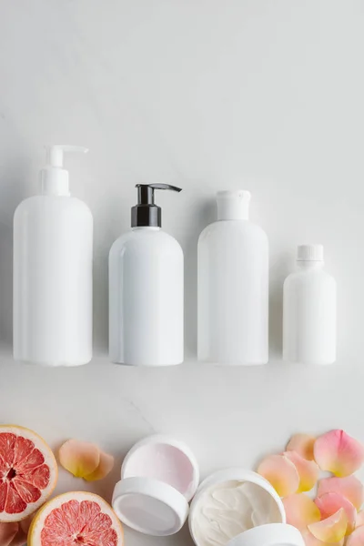 Top view of bottles of cream, pieces of grapefruit and rose petals on white surface, beauty concept — Stock Photo