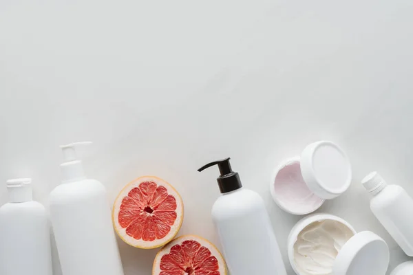 Tendido plano con recipientes de loción y trozos de pomelo sobre superficie blanca, concepto de belleza - foto de stock