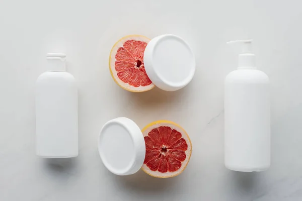 Vista elevada de botellas de crema y trozos de pomelo sobre superficie blanca, concepto de belleza - foto de stock