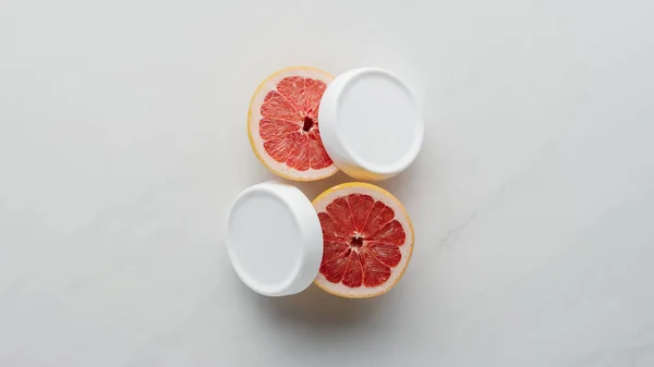 Top view of bottles of cream and pieces of grapefruit on white surface, beauty concept — Stock Photo