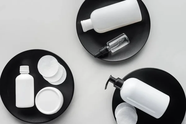 Elevated view of bottles of cream and cosmetic pads on three black plates, beauty concept — Stock Photo