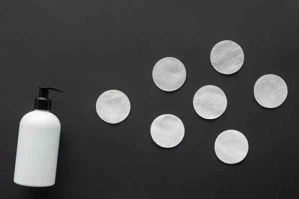 Top view of bottle of lotion and cosmetic pads isolated on black, beauty concept — Stock Photo