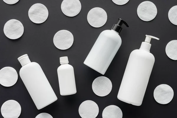 Vista superior de botellas dispersas de crema y almohadillas de algodón cosmético aisladas en negro, concepto de belleza - foto de stock