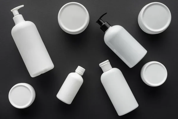 Draufsicht auf verstreute weiße Cremeflaschen, isoliert auf schwarzem, Schönheitskonzept — Stockfoto