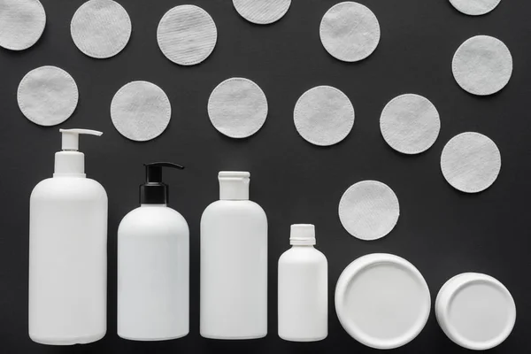 Top view of bottles of cream and cosmetic cotton pads isolated on black, beauty concept — Stock Photo