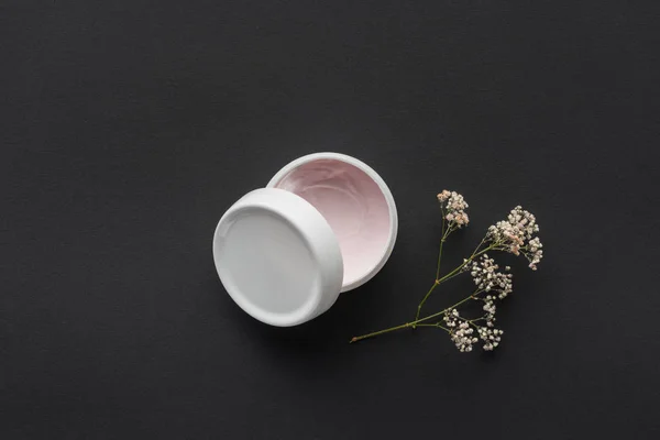 Top view of bottle of cream and dried flowers isolated on black, beauty concept — Stock Photo