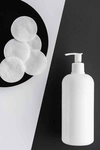 Vista dall'alto della bottiglia di crema e batuffoli di cotone sulla superficie in bianco e nero, concetto di bellezza — Foto stock