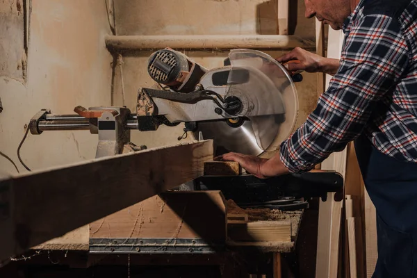 Vista parcial del carpintero usando sierra en taller de madera - foto de stock
