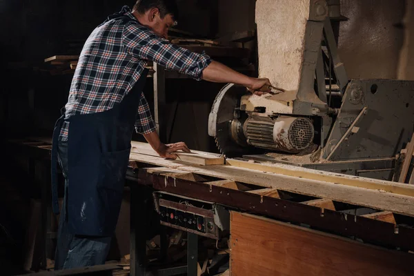 Vista lateral del carpintero usando sierra en taller de madera - foto de stock