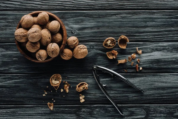 Walnuts in wooden bowl and nutcracker on dark wooden background — Stock Photo