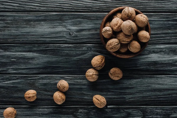 Delicious walnuts in wooden bowl on dark wooden tabletop — Stock Photo